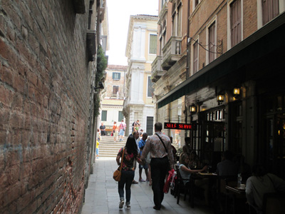 4 photos show an alley about 15 feet wide, with tables and chairs for a cafe along one side, and at the end of the buildings we see a set of stairs with about 7 steps going up.